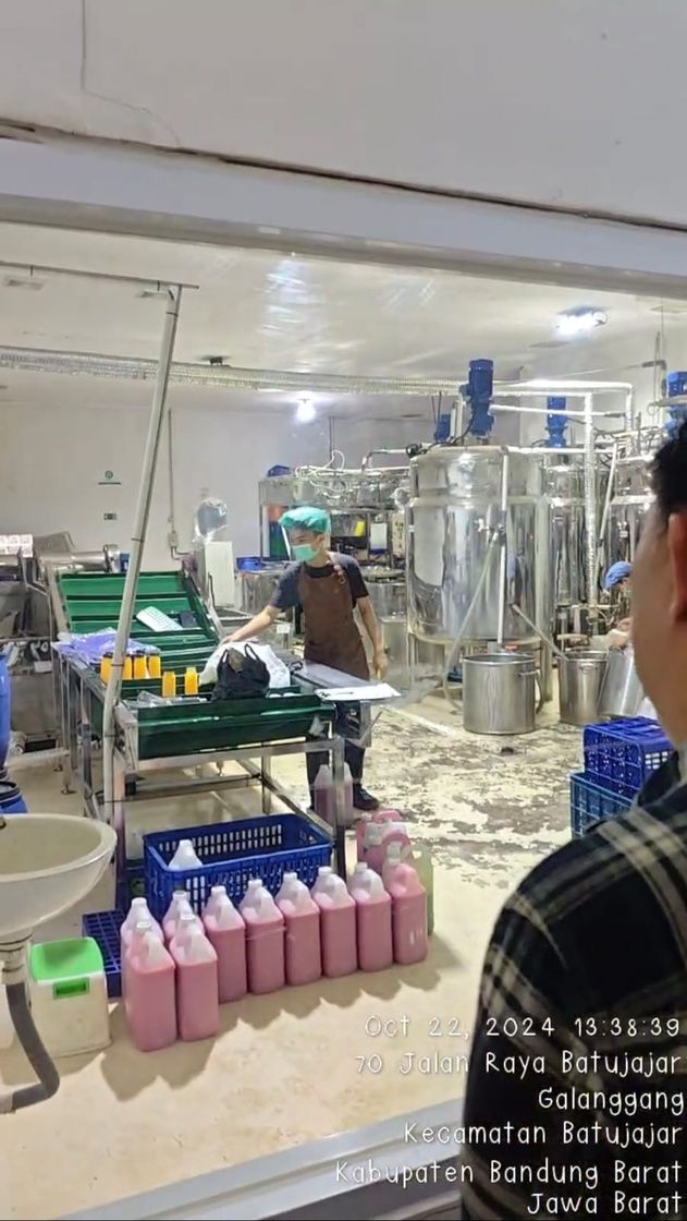 Ruang produksi dengan tangki stainless dan botol jus merah muda siap kemas